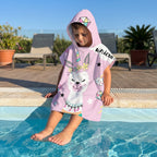 Poncho serviette a capuche motif lama licorne, porte par un enfant assis au bord d'une piscine.