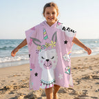 Poncho serviette a capuche motif lama licorne, porte par une enfant souriante sur la plage.