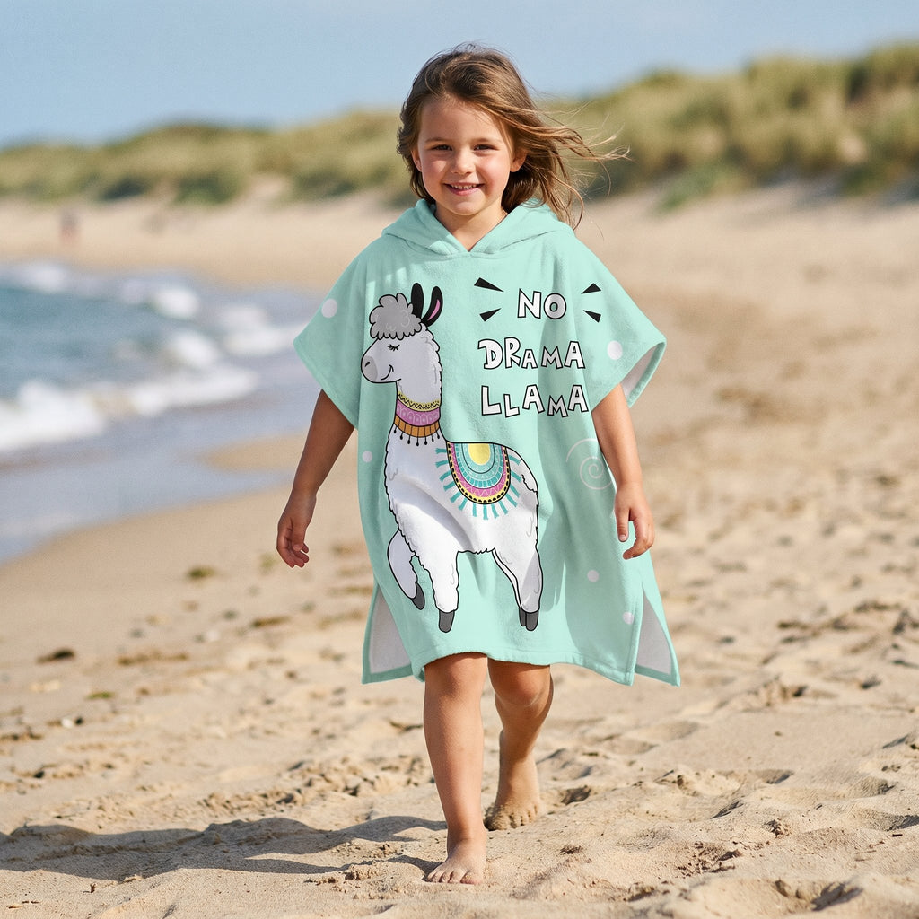 Poncho serviette à capuche motif lama menthe, porté par une enfant marchant sur la plage.