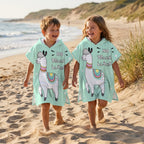 Poncho serviette à capuche motif lama menthe, porté par deux enfants marchant côte à côte sur la plage.