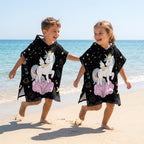 Poncho serviette a capuche motif licorne étoilée, porté par deux enfants joyeux sur le sable.