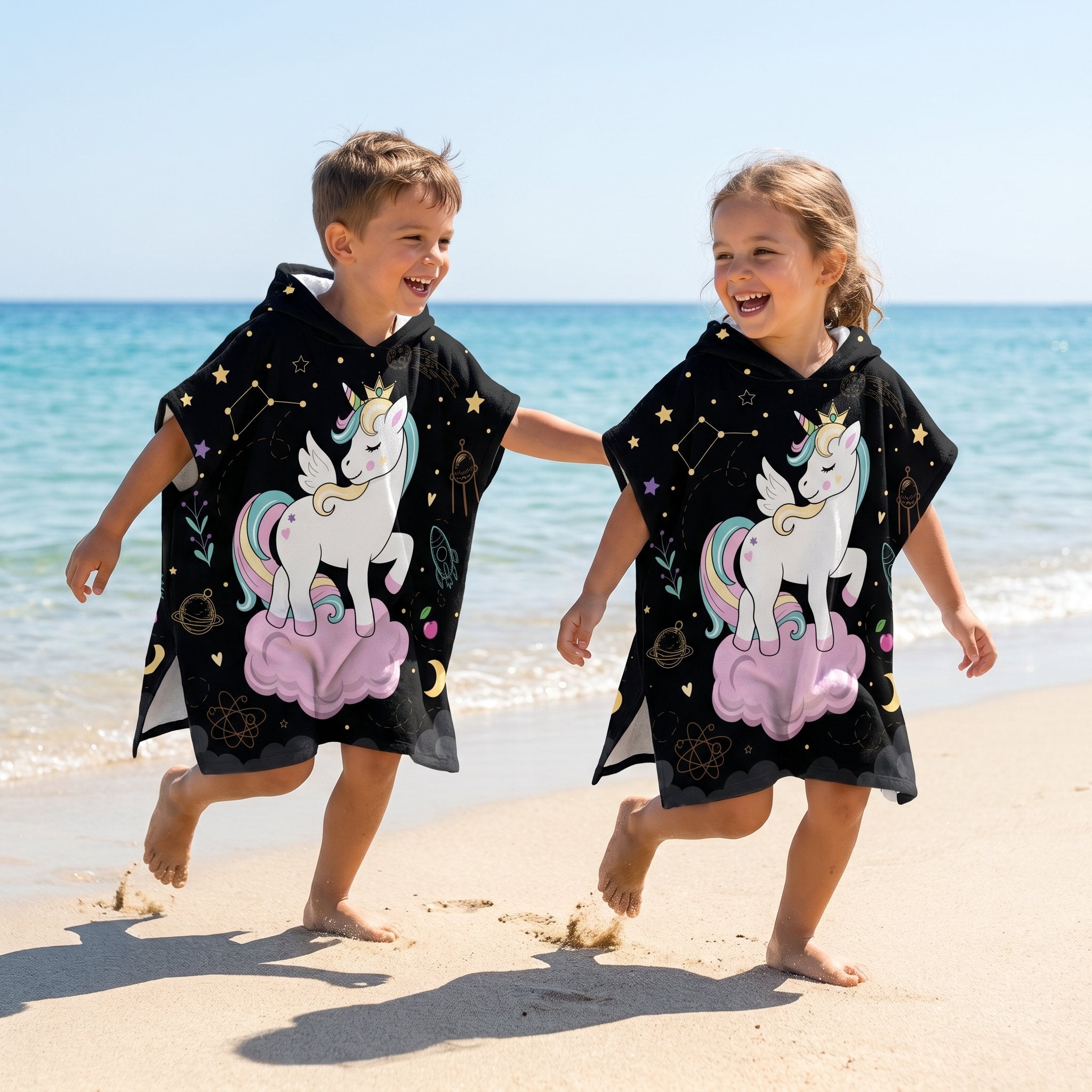 Poncho serviette a capuche motif licorne étoilée, porté par deux enfants joyeux sur le sable.