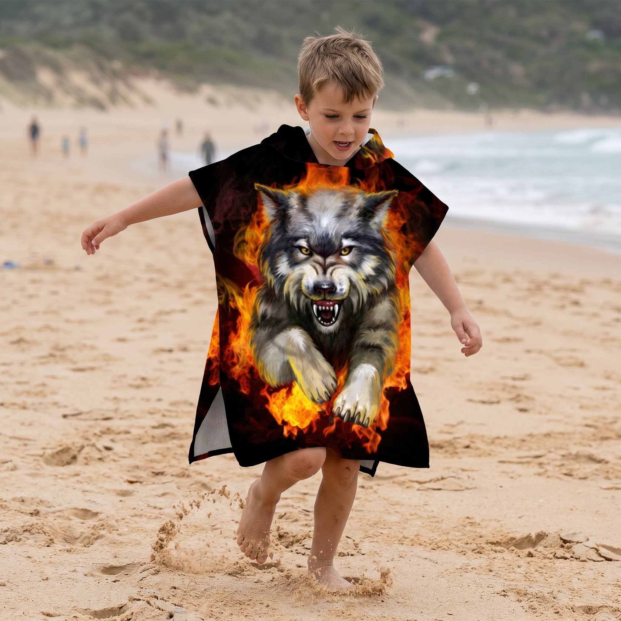 Poncho serviette a capuche motif Loup de feu, porte par un enfant courant sur la plage.
