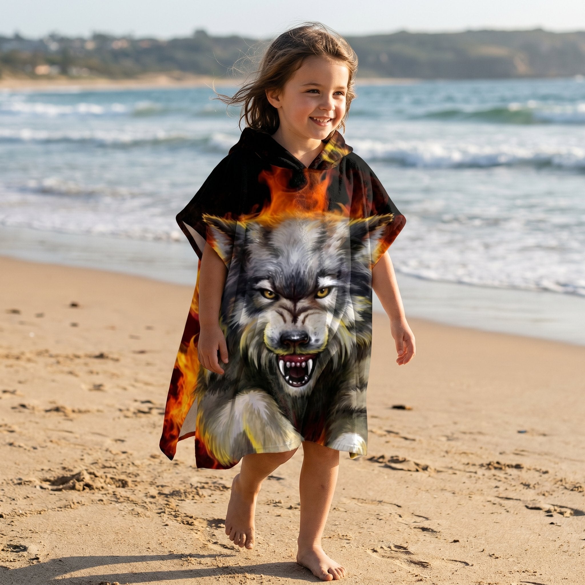 Poncho serviette a capuche motif Loup de feu, porte par une enfant souriante sur la plage.