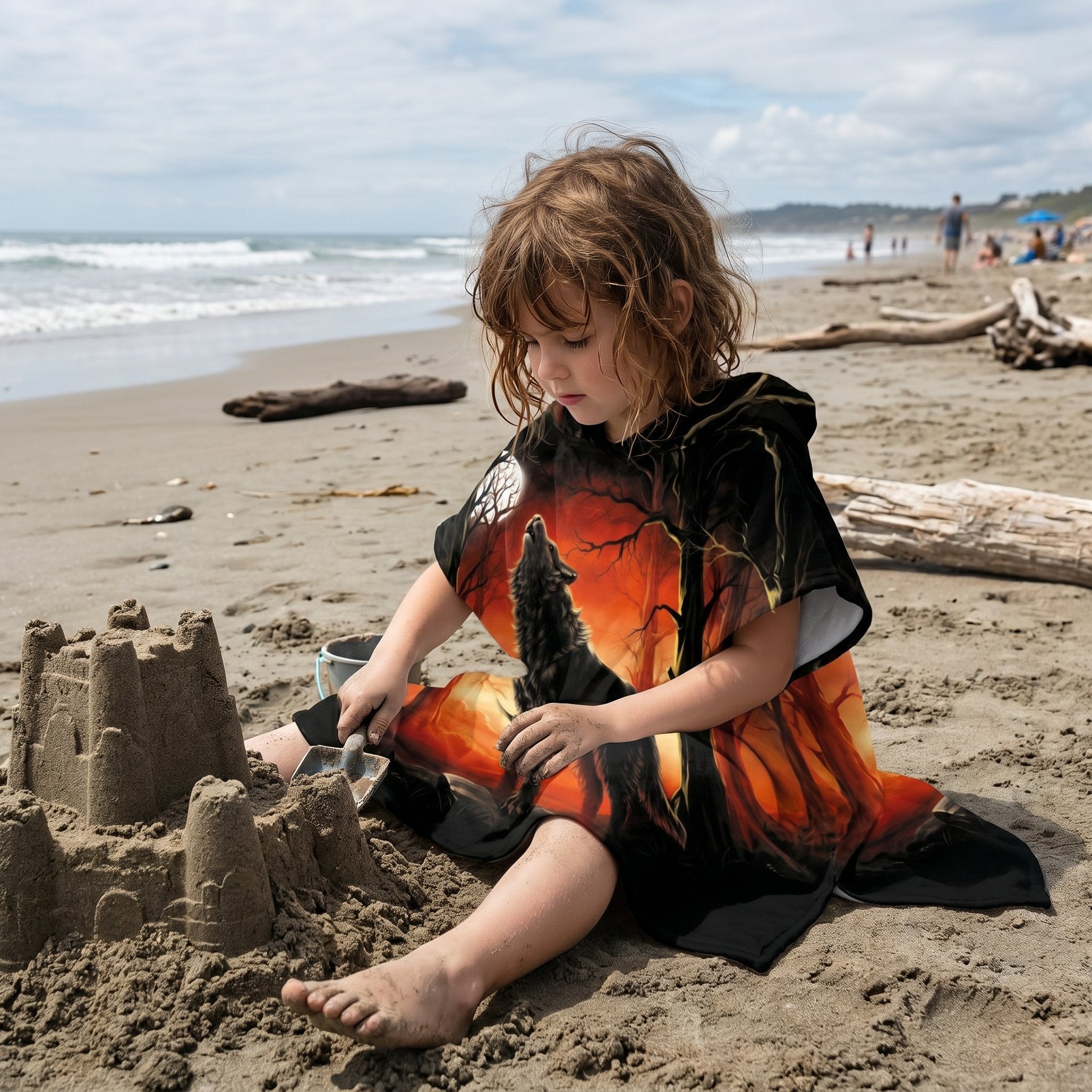 Poncho serviette a capuche motif loup forêt rouge porté par un enfant assis sur la plage.