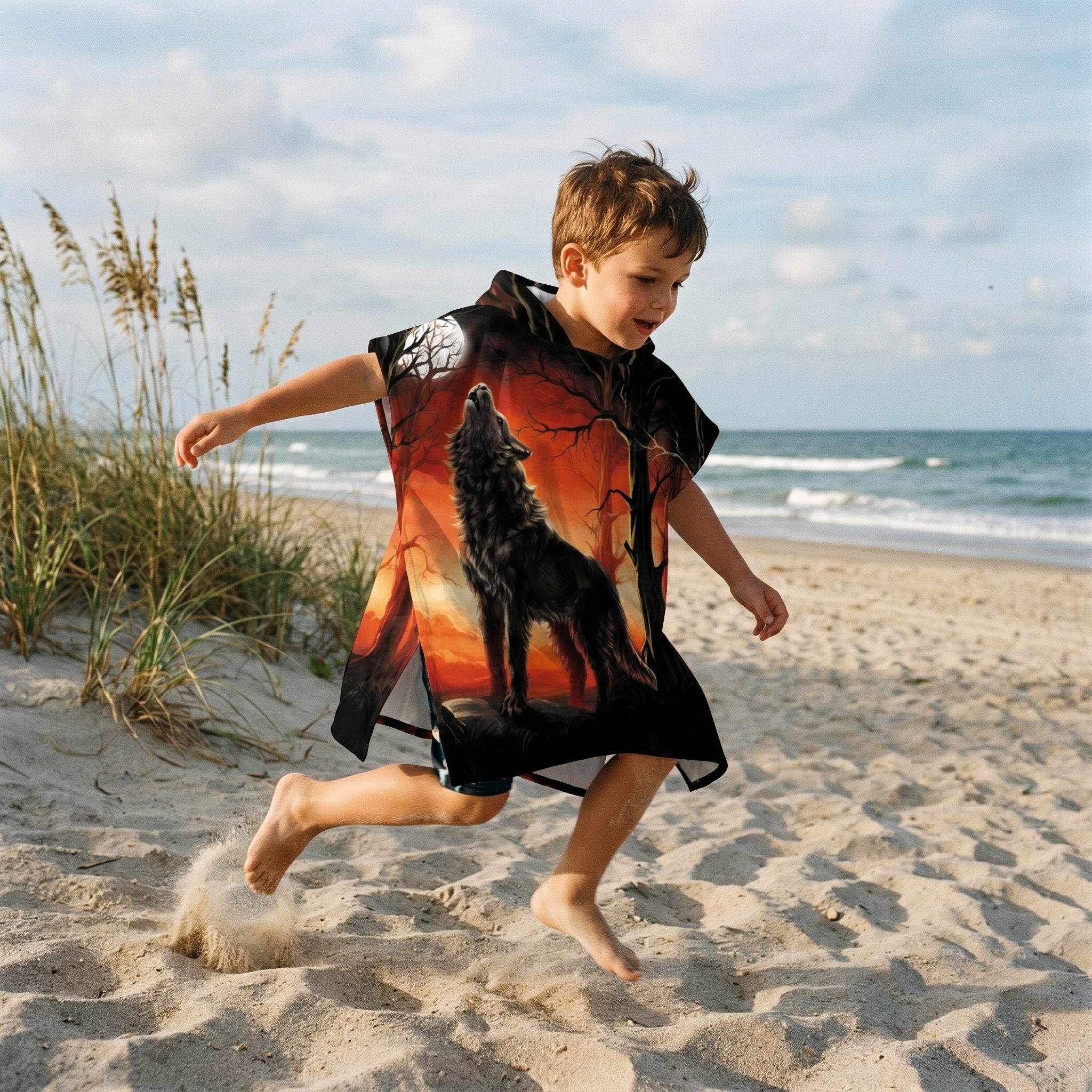 Poncho serviette a capuche motif loup forêt rouge porté par un enfant sautant joyeusement sur la plage.