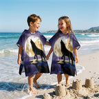 Poncho serviette a capuche motif loup lune violette, porte par deux enfants jouant au bord de l'eau.