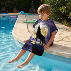 Poncho serviette a capuche motif loup lune violette, porte par un enfant assis au bord d'une piscine.
