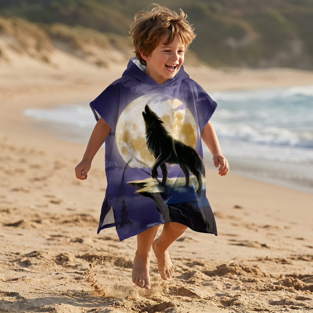 Poncho serviette a capuche motif loup lune violette, porte par un enfant sautant de joie sur le sable.