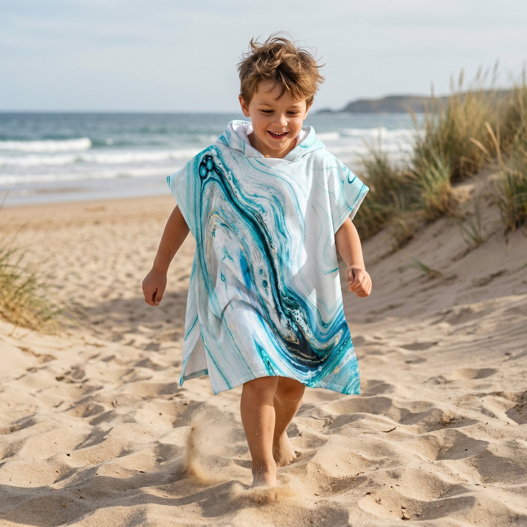 Poncho serviette a capuche motif marbre bleu ciel, porté par un enfant courant joyeusement sur le sable fin de la plage.