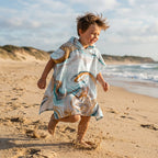 Poncho serviette a capuche motif marbre cuivré, porté par un enfant courant joyeusement sur la plage.