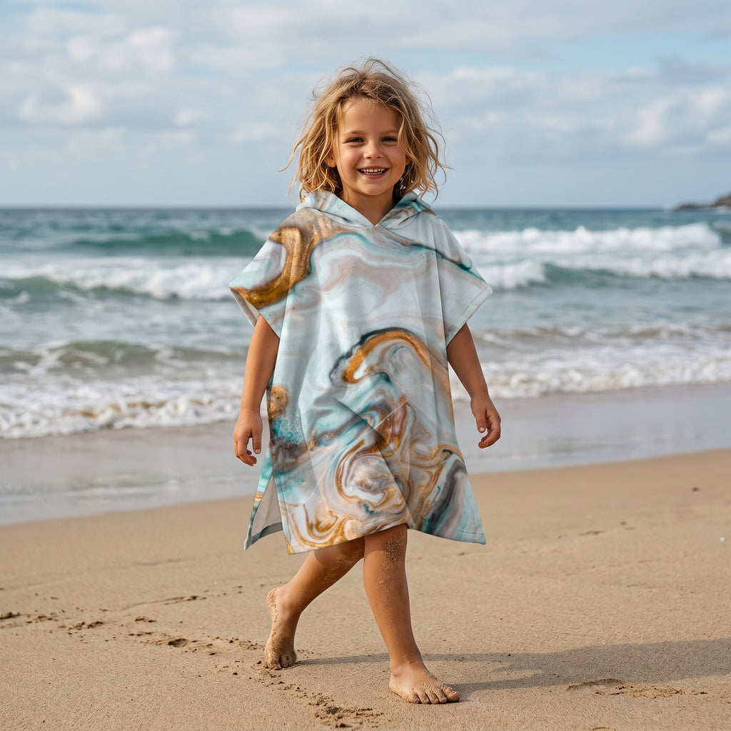 Poncho serviette a capuche motif marbre cuivré, porté par un enfant marchant face à la mer.