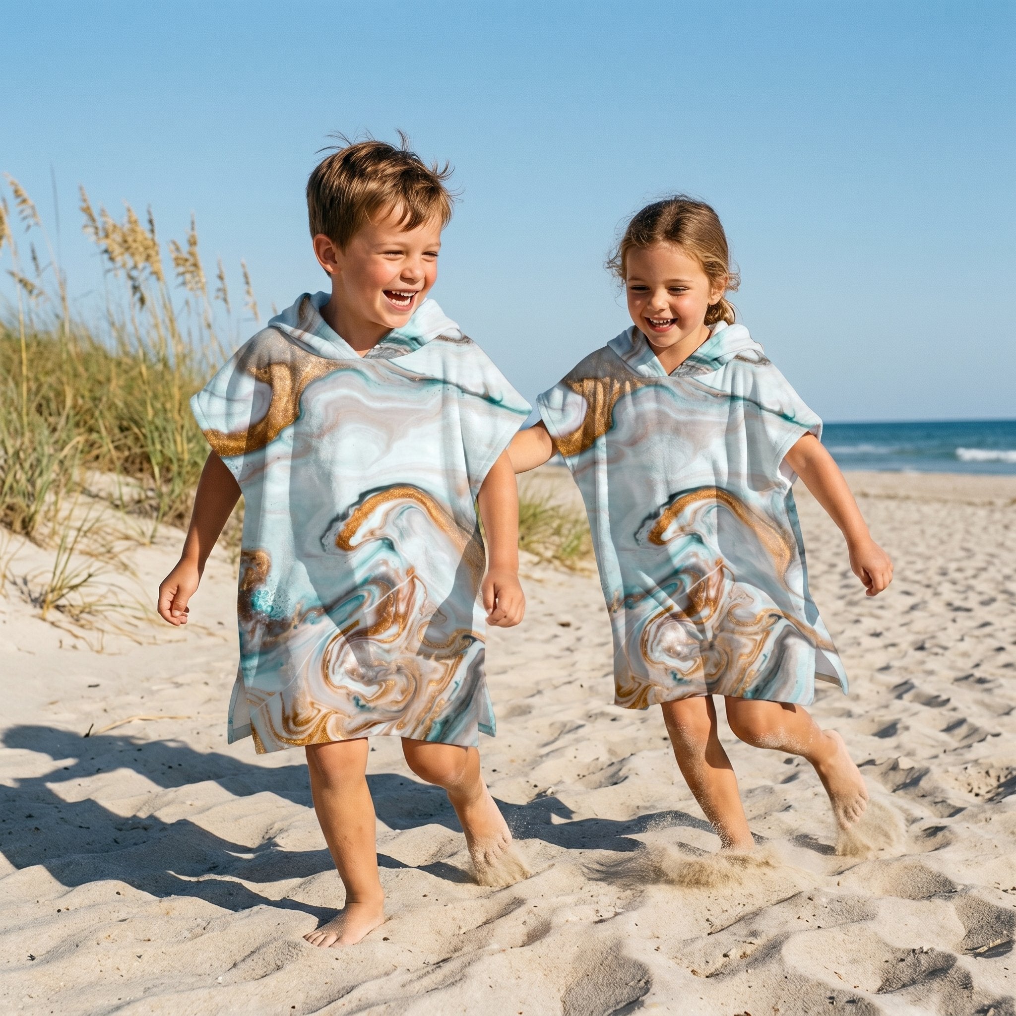 Poncho serviette a capuche motif marbre cuivré, porté par deux enfants courant ensemble sur le sable.