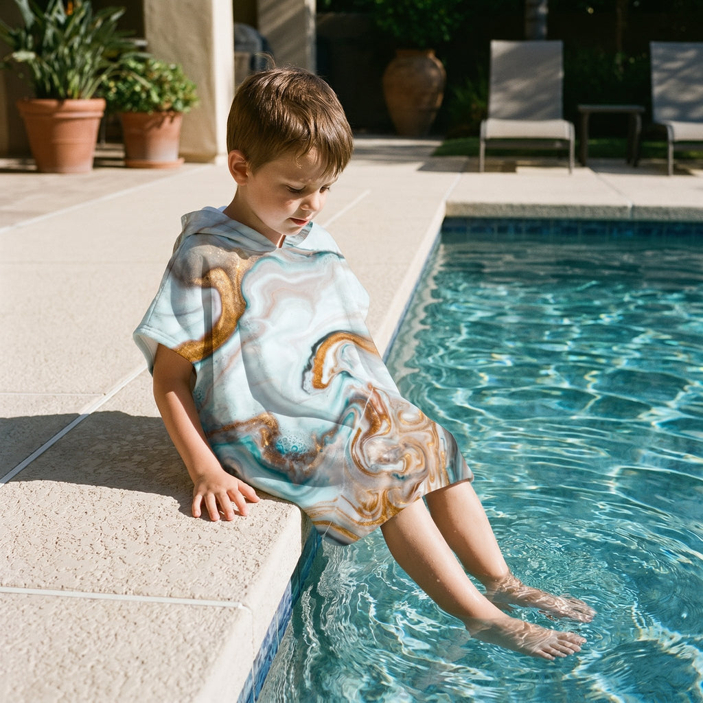 Poncho serviette a capuche motif marbre cuivré, porté par un enfant assis au bord d'une piscine.