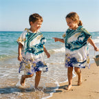 Poncho serviette a capuche motif marbre nuit dorée, porte par deux enfants rieurs au bord de l'eau.