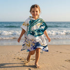 Poncho serviette a capuche motif marbre nuit dorée, porte par une fille souriante marchant sur le sable.