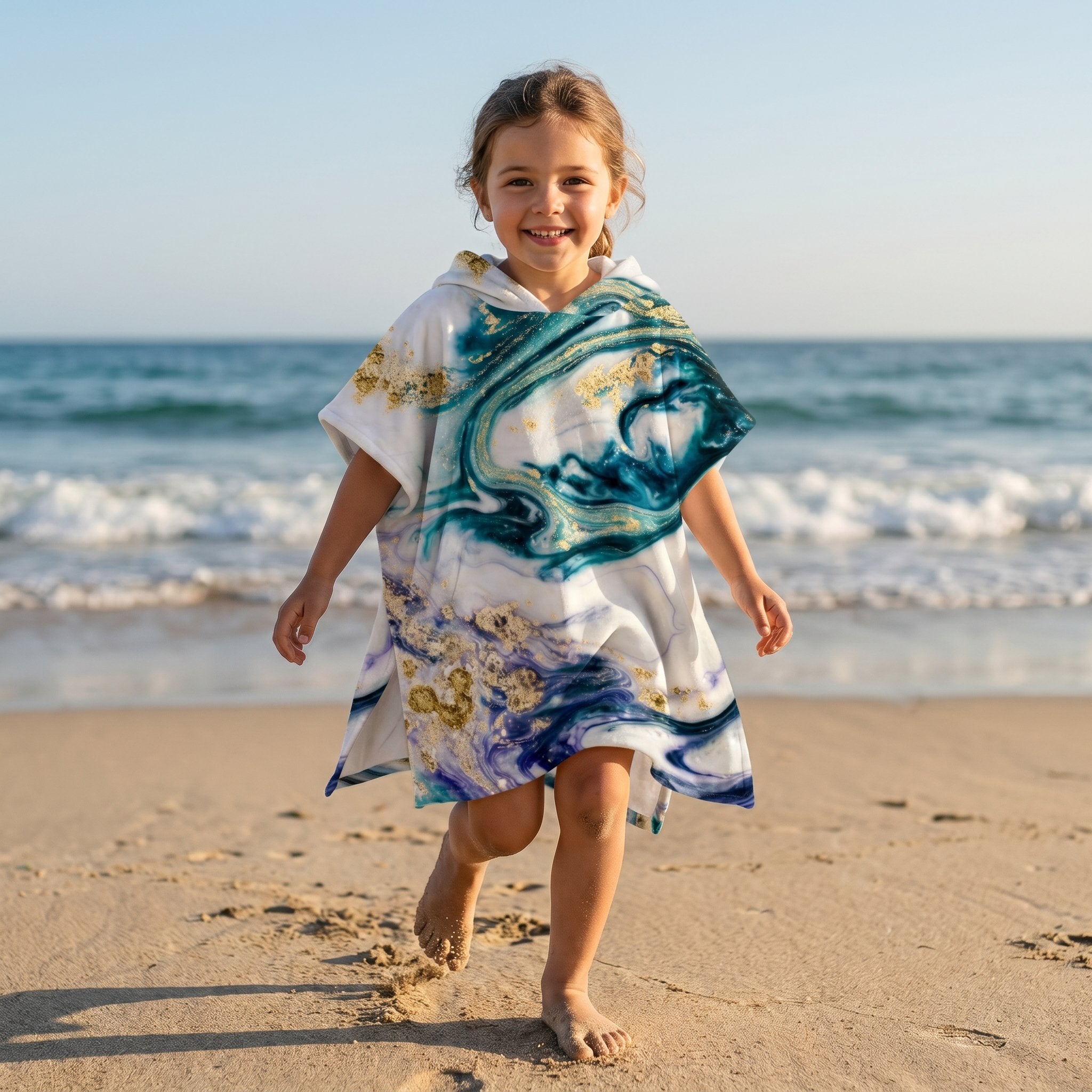 Poncho serviette a capuche motif marbre nuit dorée, porte par une fille souriante marchant sur le sable.