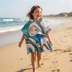 Poncho serviette a capuche motif marbre tourbillon cuivré, porté par une enfant souriante courant sur le sable.