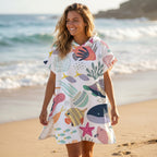 Poncho serviette a capuche motif Fonds marins colorés, porté par une femme souriante marchant au bord de l'eau.