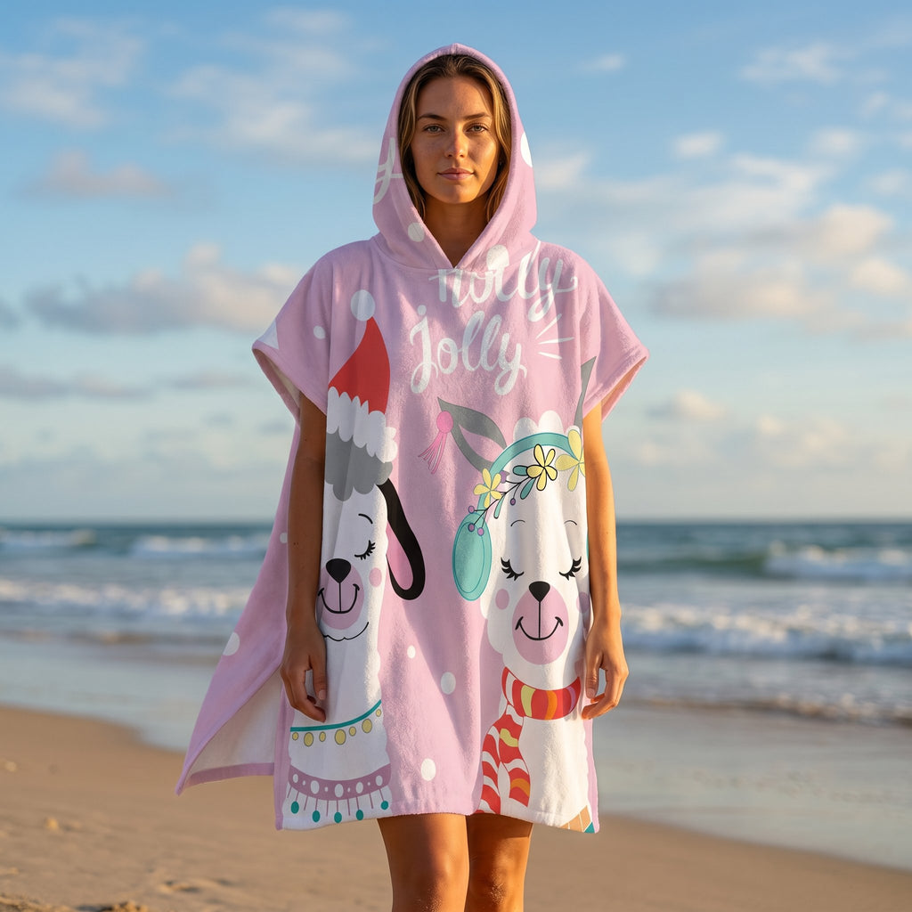 Poncho serviette à capuche motif lamas de Noël, porté par une femme debout sur une plage face à l'océan.