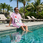 Poncho serviette à capuche motif lamas de Noël, porté par un homme assis au bord d'une piscine.
