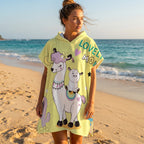 Poncho serviette à capuche motif lamas et cactus, porté par une femme sur une plage ensoleillée, vue de face.