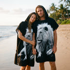 Poncho serviette à capuche motif lion noir et blanc, porté par un couple sur la plage.