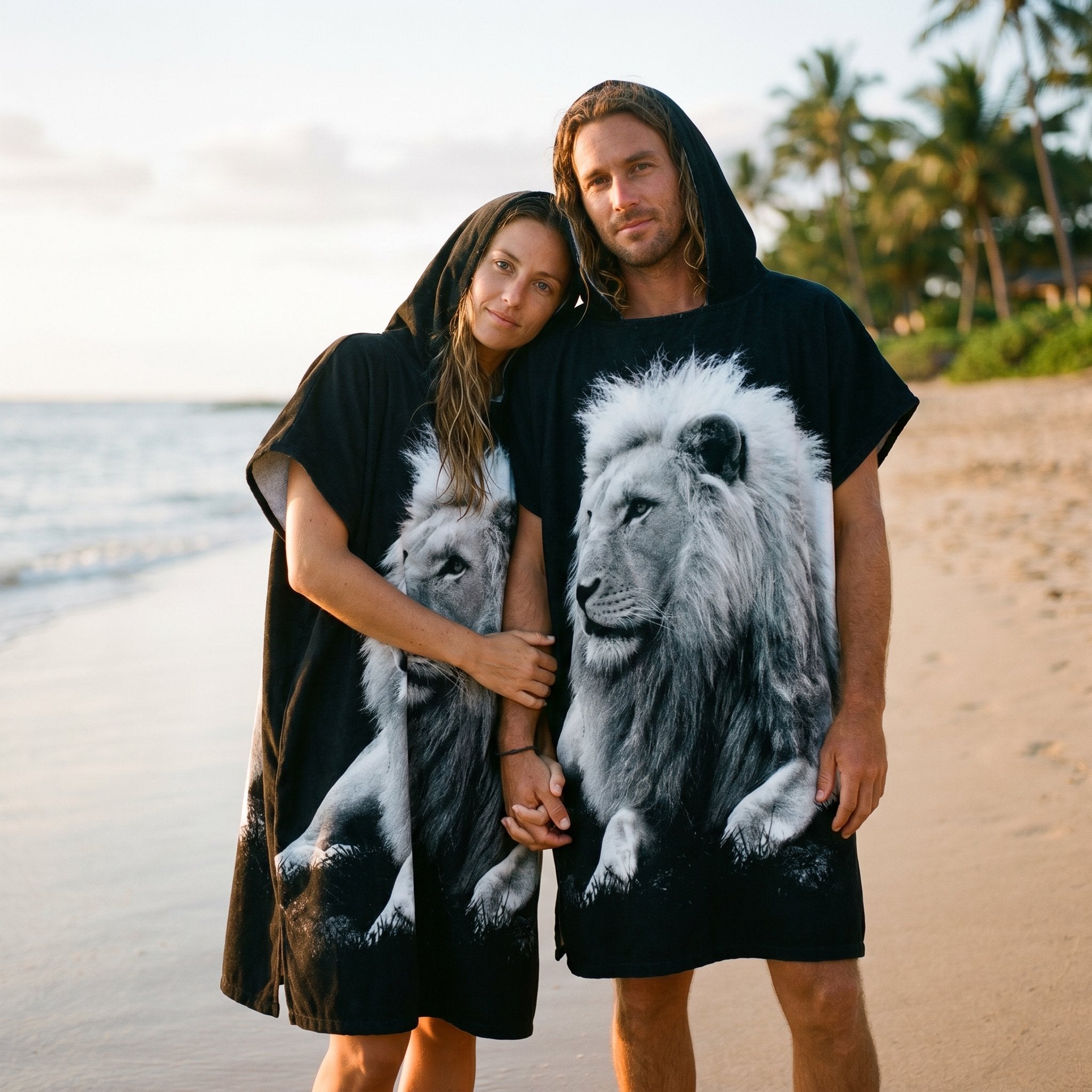 Poncho serviette à capuche motif lion noir et blanc, porté par un couple sur la plage.