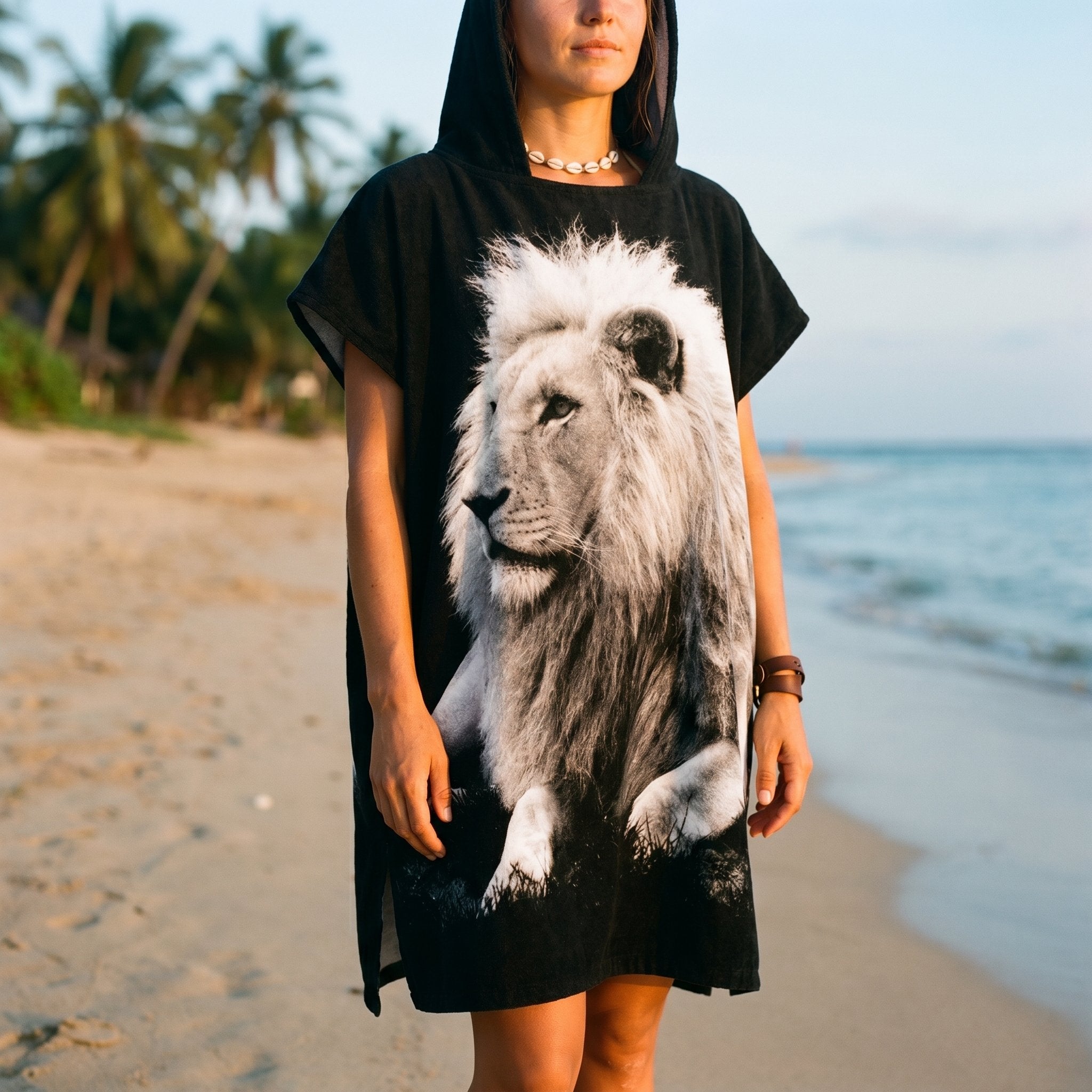 Poncho serviette à capuche motif lion noir et blanc, porté par une femme en plan moyen sur la plage.