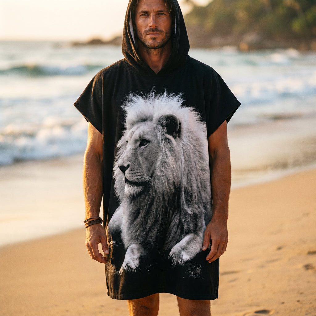 Poncho serviette à capuche motif lion noir et blanc, porté par un homme en plan large sur la plage.