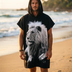 Poncho serviette à capuche motif lion noir et blanc, porté par un homme en plan large sur la plage.