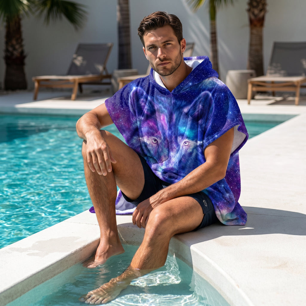 Poncho serviette a capuche motif Loup cosmos violet, porté par un homme assis au bord d'une piscine, les pieds dans l'eau.