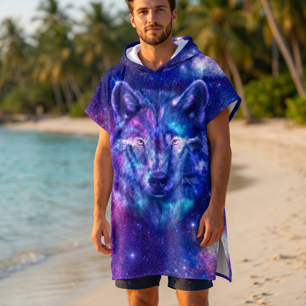 Poncho serviette a capuche motif Loup cosmos violet, porté par un homme debout sur une plage de sable fin, face a l'objectif.