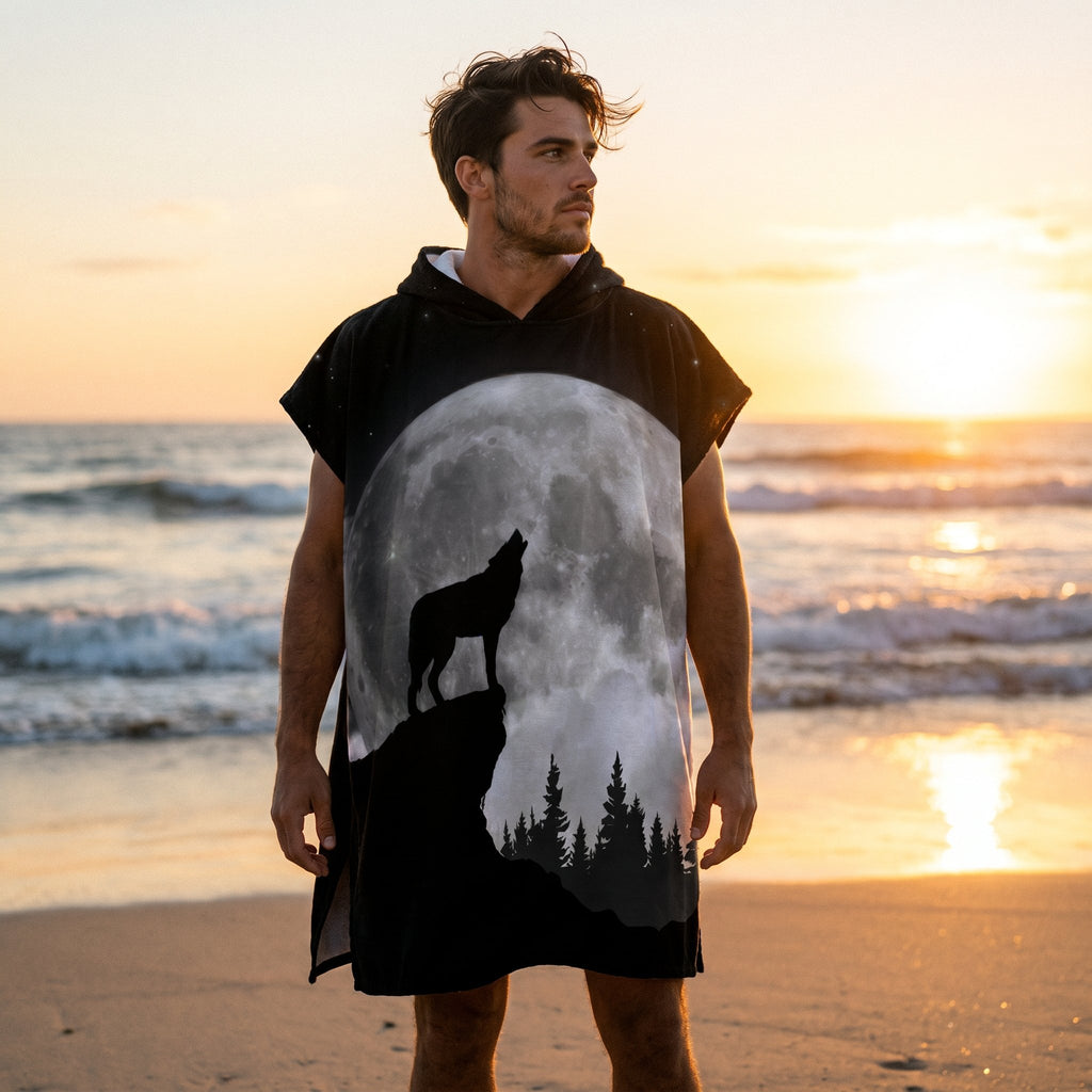 Poncho serviette à capuche motif loup et lune, porté par un homme sur une plage au coucher du soleil, vu de face.