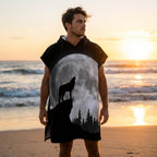 Poncho serviette à capuche motif loup et lune, porté par un homme sur une plage au coucher du soleil, vu de face.