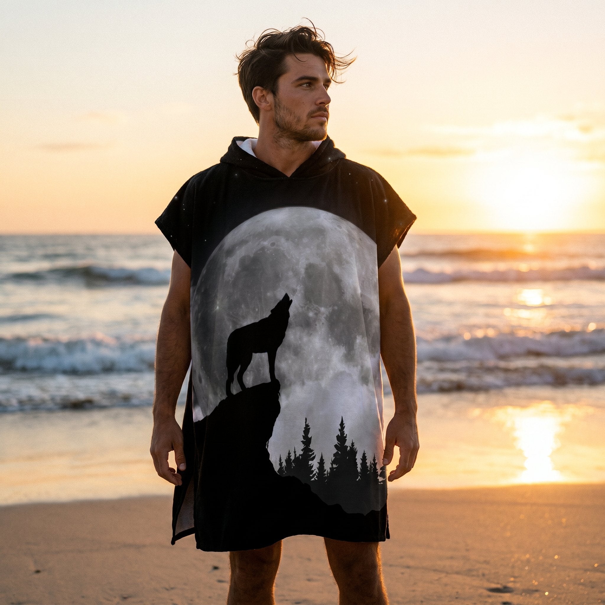 Poncho serviette à capuche motif loup et lune, porté par un homme sur une plage au coucher du soleil, vu de face.