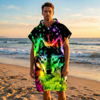 Poncho serviette à capuche motif Loup néon, porté par un homme debout sur une plage au coucher du soleil.