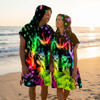 Poncho serviette à capuche motif Loup néon, porté par un couple souriant se tenant la main sur la plage.