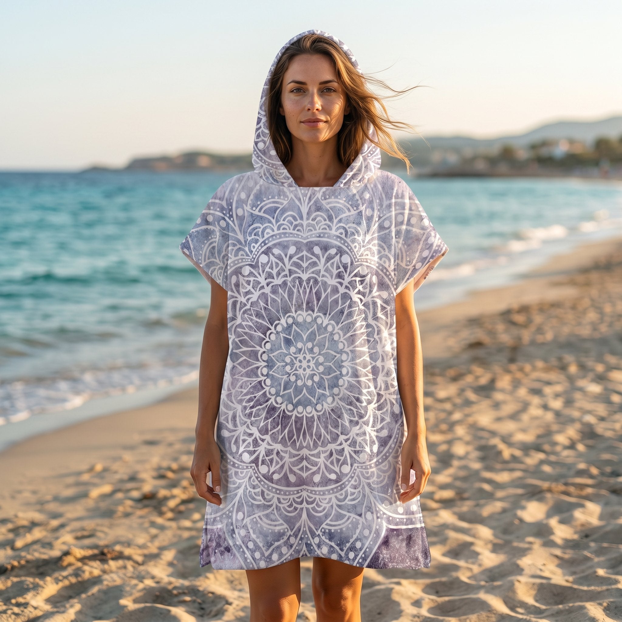 Poncho serviette à capuche motif mandala dentelle violet porté par une femme sur une plage de sable.