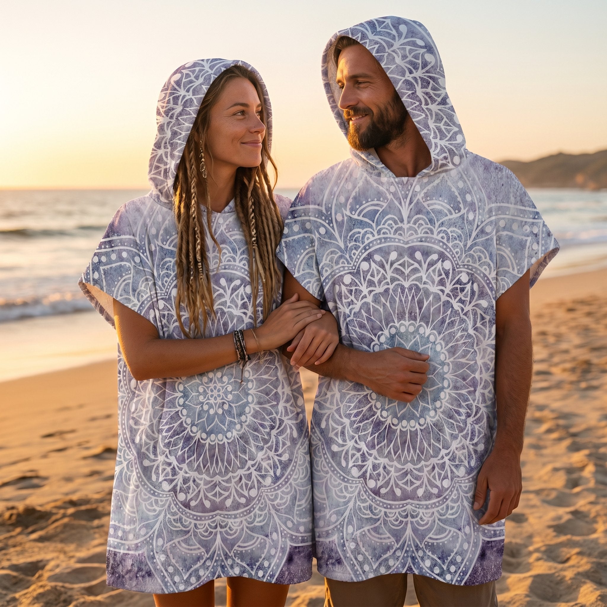 Poncho serviette à capuche motif mandala dentelle violet porté par un couple sur une plage au soleil couchant.