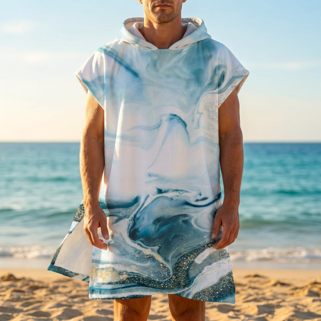 Poncho serviette a capuche motif marbre bleu givré, porté par un homme de face, debout sur le sable près de l'océan.