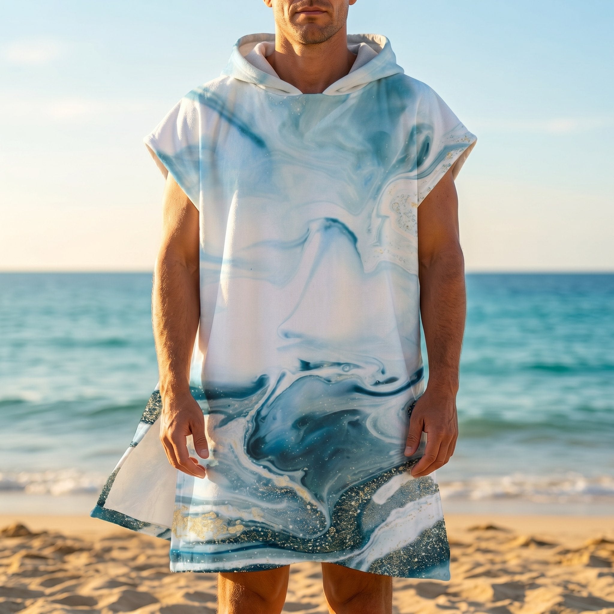 Poncho serviette a capuche motif marbre bleu givré, porté par un homme de face, debout sur le sable près de l'océan.