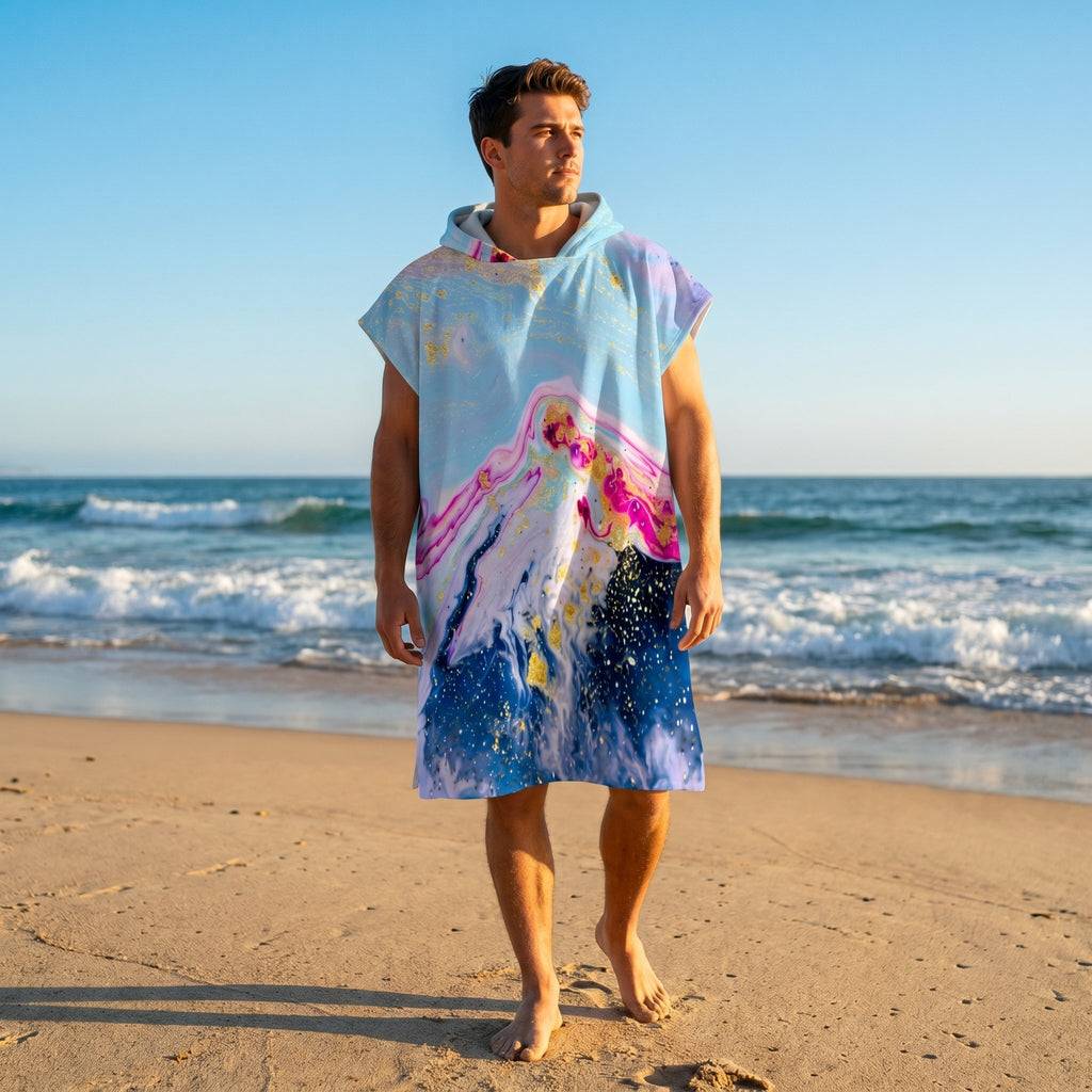 Poncho serviette a capuche motif marbre montagne rose, porte par un homme debout face a l'ocean.