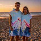 Poncho serviette a capuche motif marbre montagne rose, porte par un couple debout sur le sable au soleil couchant.