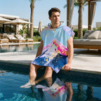 Poncho serviette a capuche motif marbre montagne rose, porte par un homme les pieds dans l'eau de la piscine.