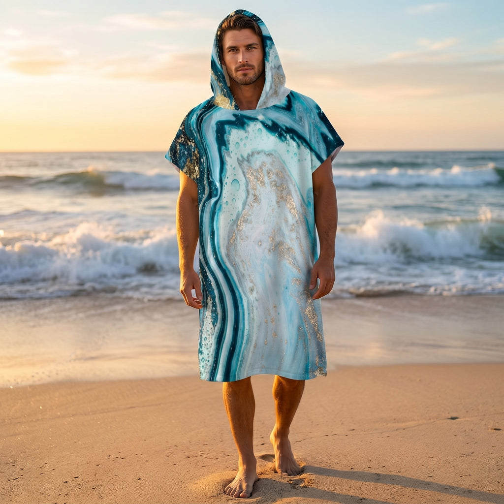 Poncho serviette à capuche motif marbre turquoise doré, porté par un homme sur une plage au coucher du soleil.