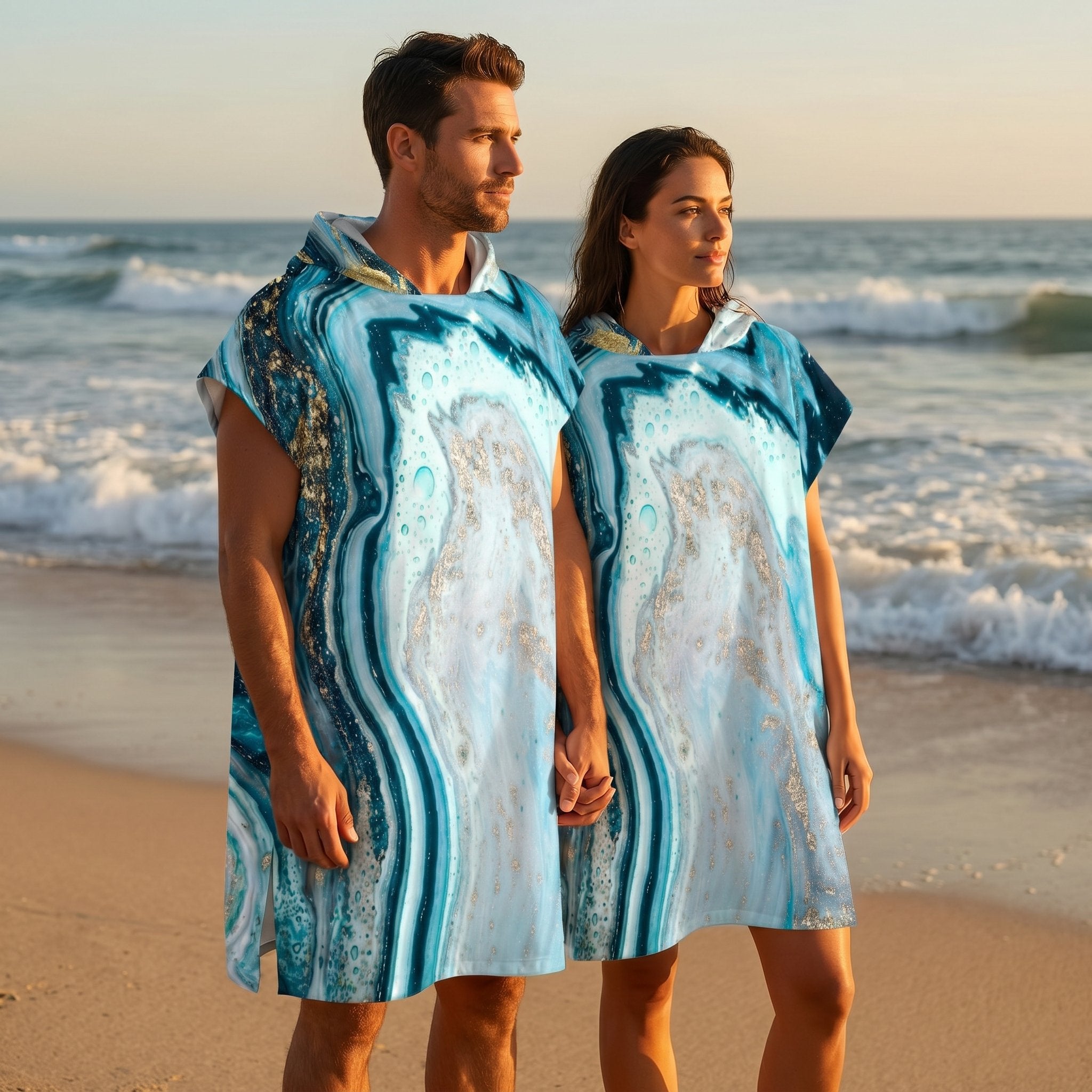 Poncho serviette à capuche motif marbre turquoise doré, porté par un couple se tenant la main sur la plage.