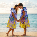 Poncho serviette à capuche motif oiseau peint, porté par un couple se tenant la main sur la plage.