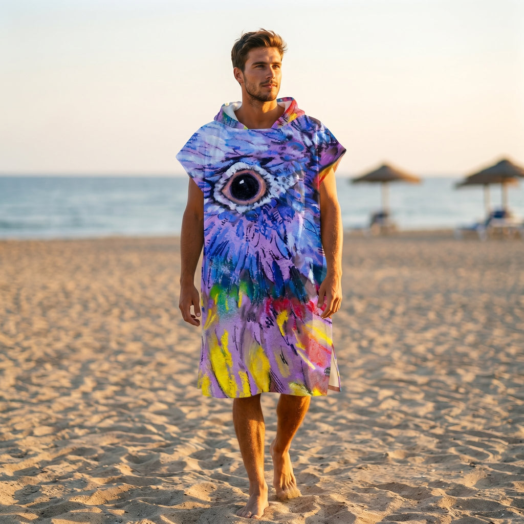 Poncho serviette à capuche motif oiseau peint, porté par un homme marchant seul sur le sable de la plage.