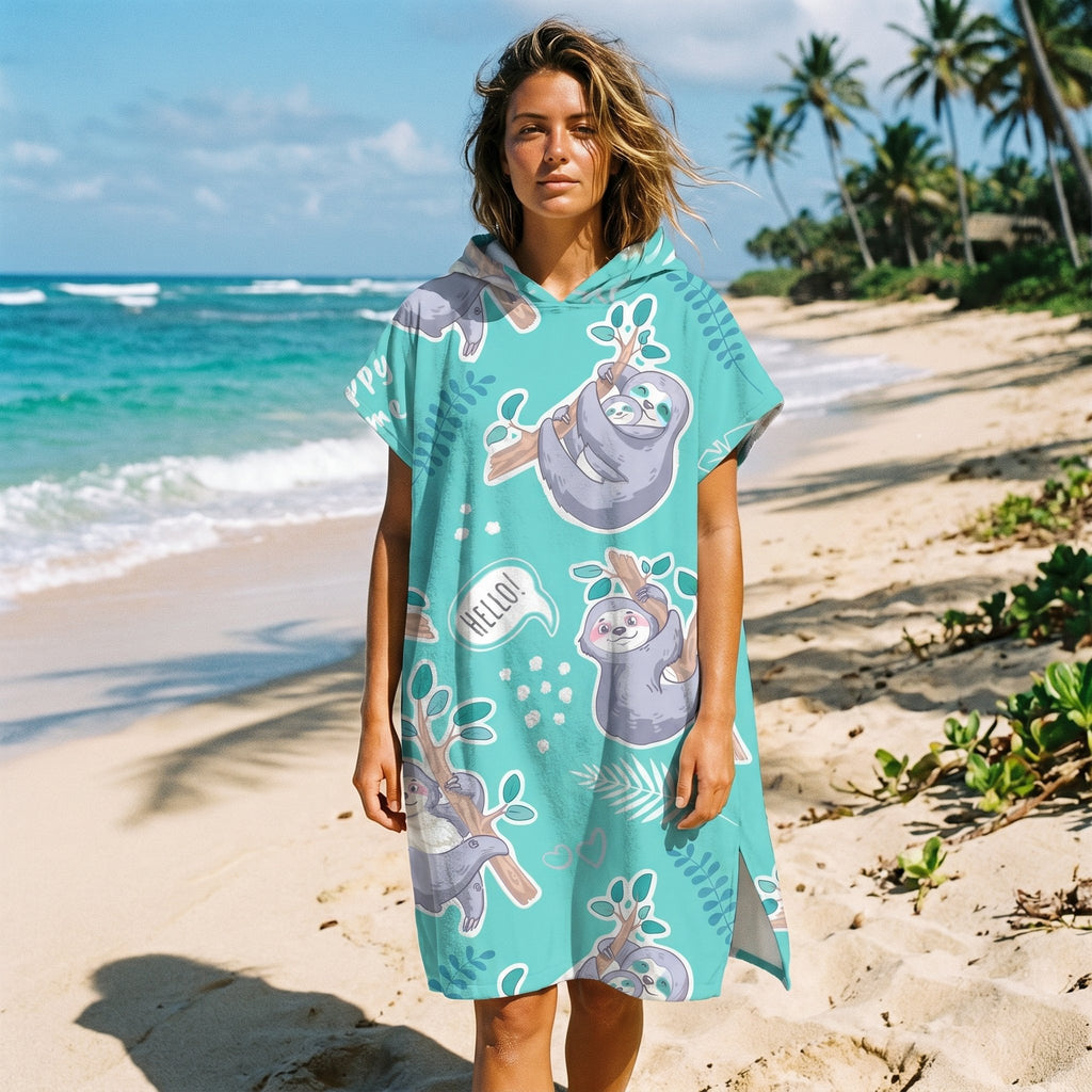 Poncho serviette a capuche motif paresseux turquoise, porte par une femme debout sur une plage ensoleillee.